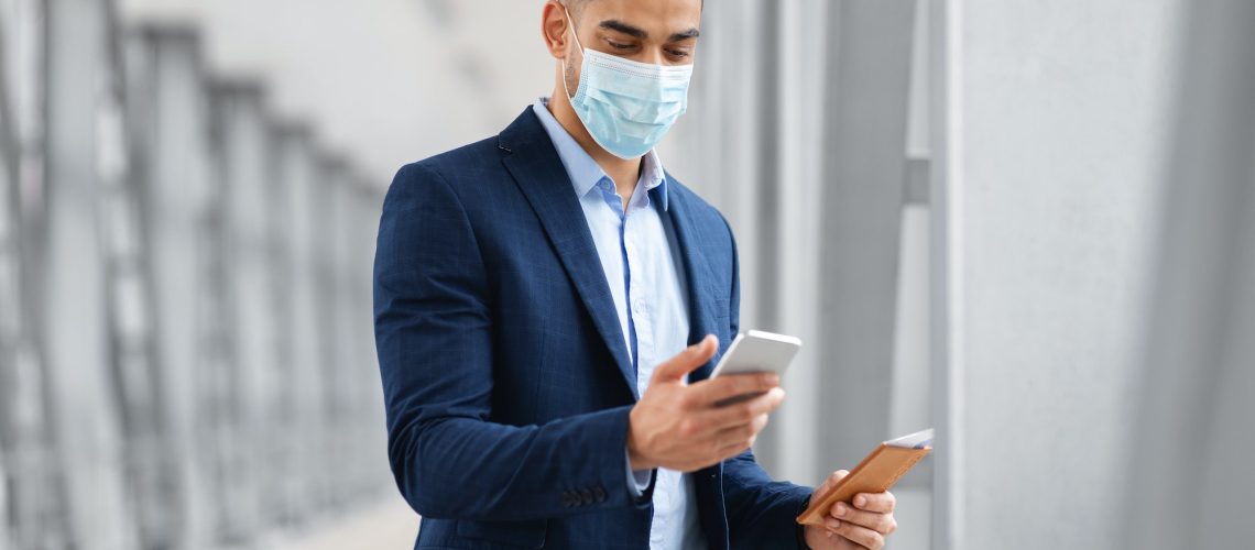 middle-eastern-businessman-wearing-medical-mask-using-smartphone-at-airport
