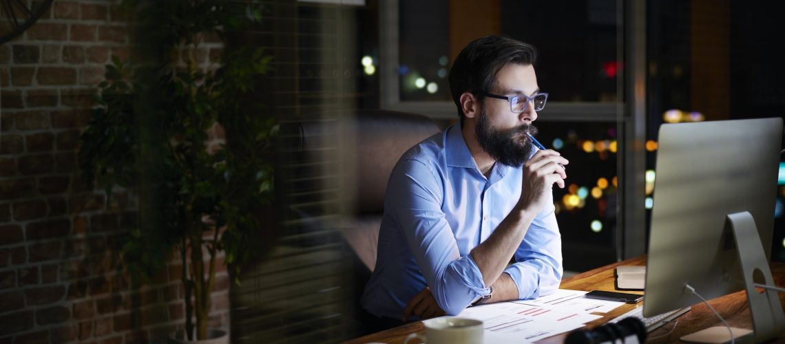 young-businessman-looking-at-computer-on-office-desk-at-night