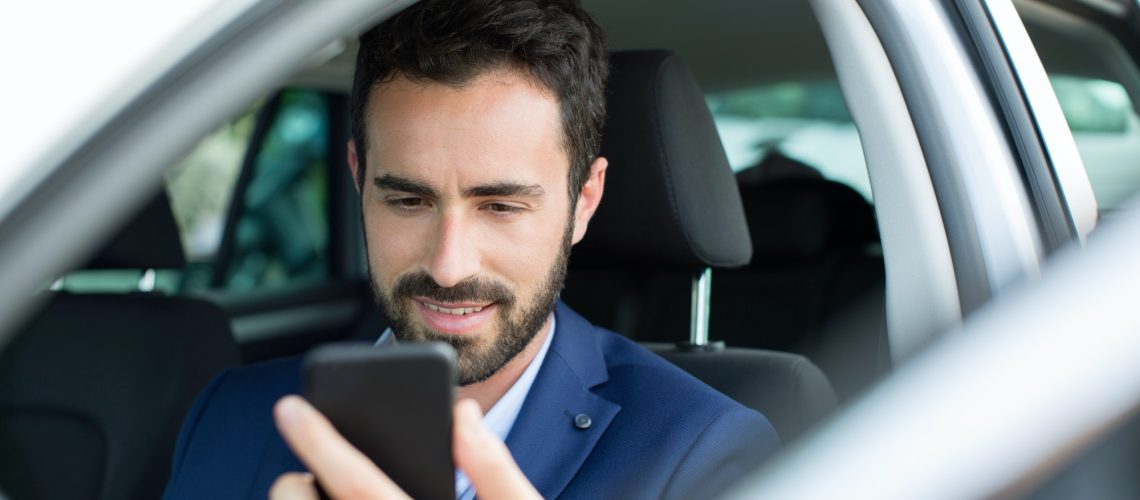 young-businessman-reading-smartphone-texts-in-car